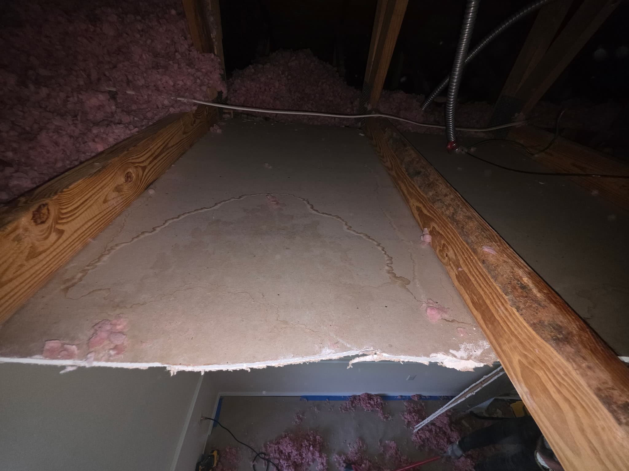 Attic view down onto the back of a ceiling, showing a large water stain spreading across the drywall between two joists